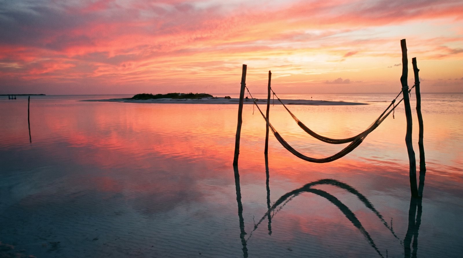 Atardecer rosado reflejado en el agua somera de Holbox con una hamaca sobre el mar